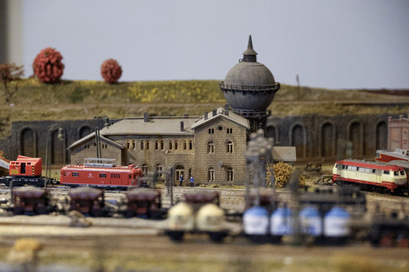 Modelbahnanlage mit einem Bahnhof, roten Zügen und historischen Gebäuden.