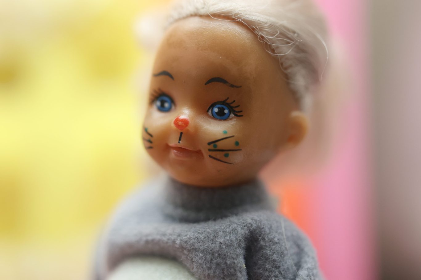 Puppe mit blauen Augen und Katzenhaaren, trägt einen grauen Pullover.