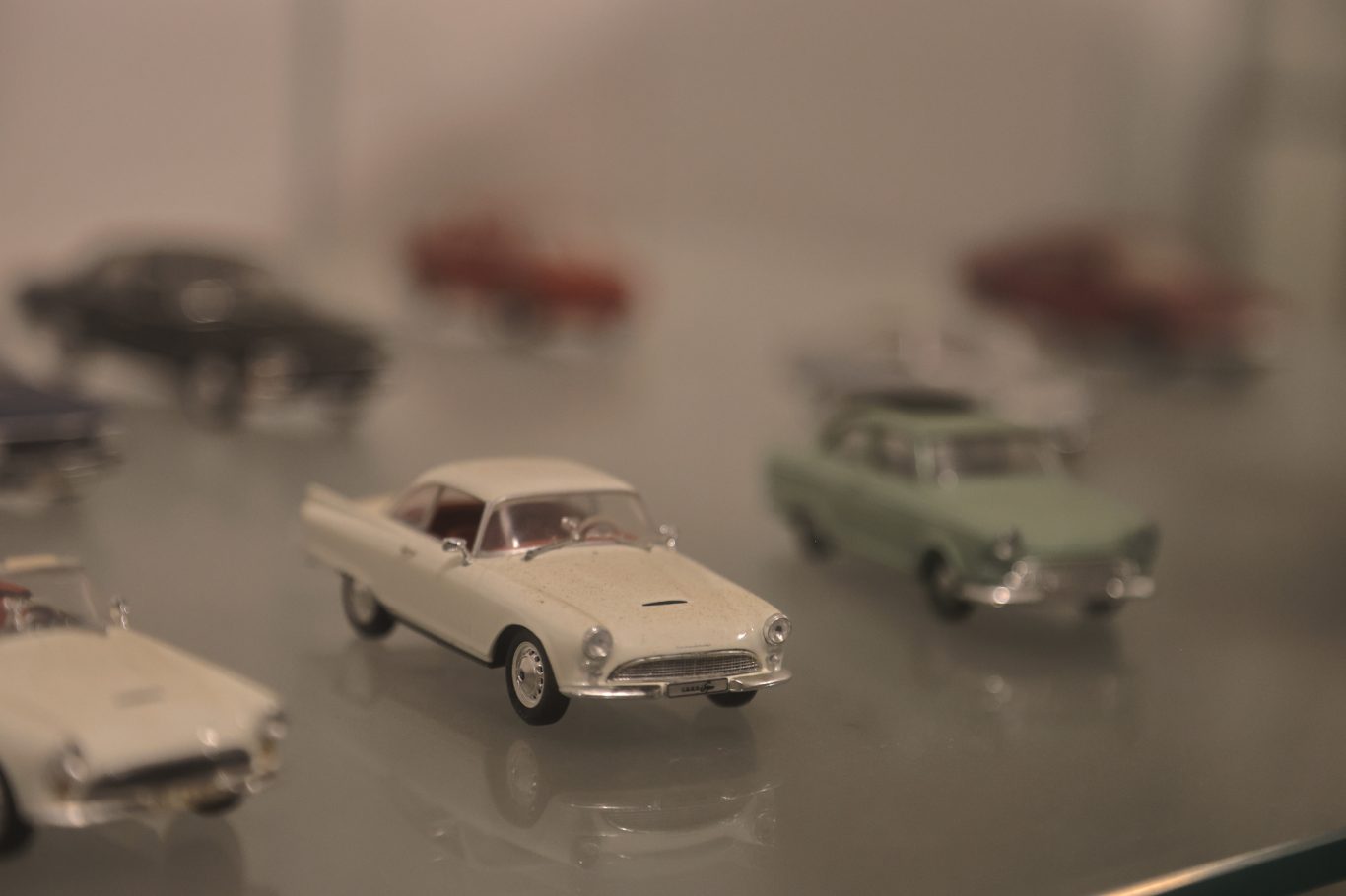 Verschiedene Modellautos in einer Glasvitrine, darunter ein weißes und ein grünes Auto.