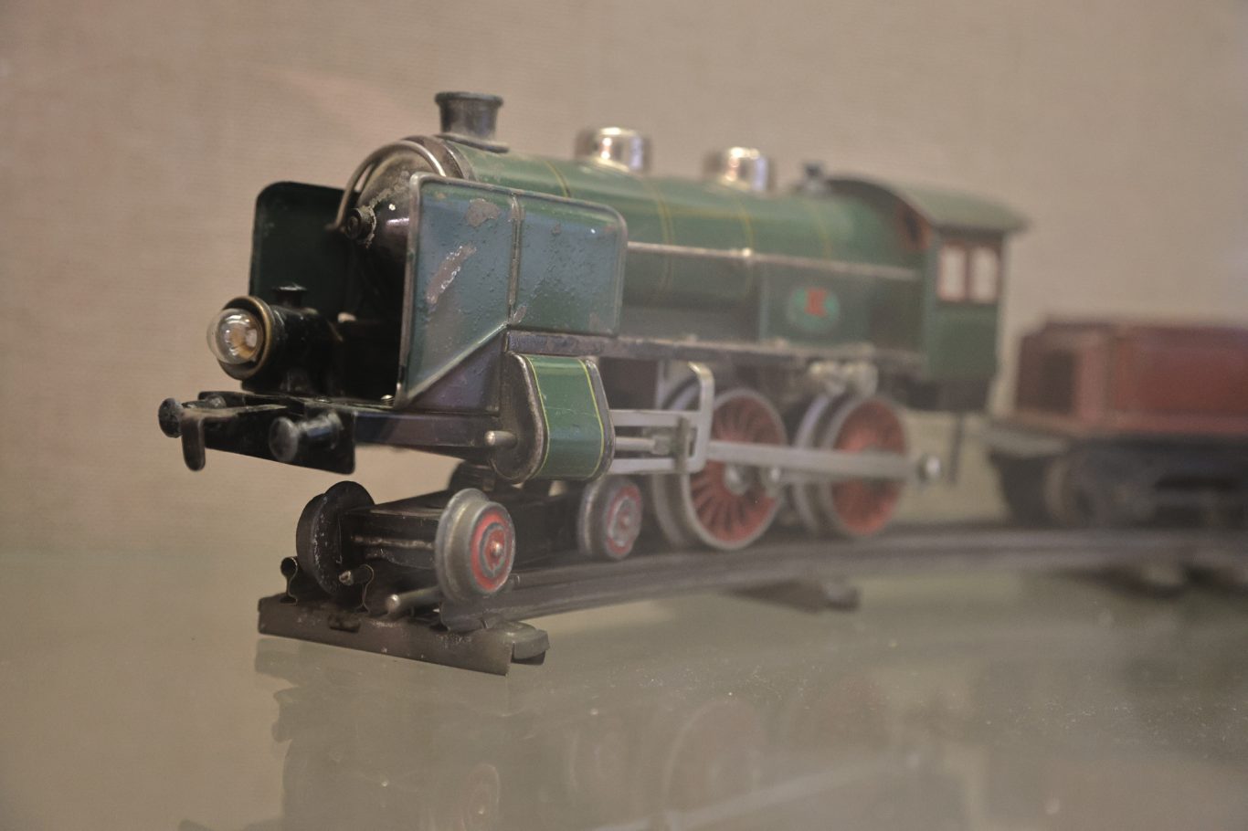 Grüne Lokomotive mit roten Rädern und einem Waggon auf Schienen.