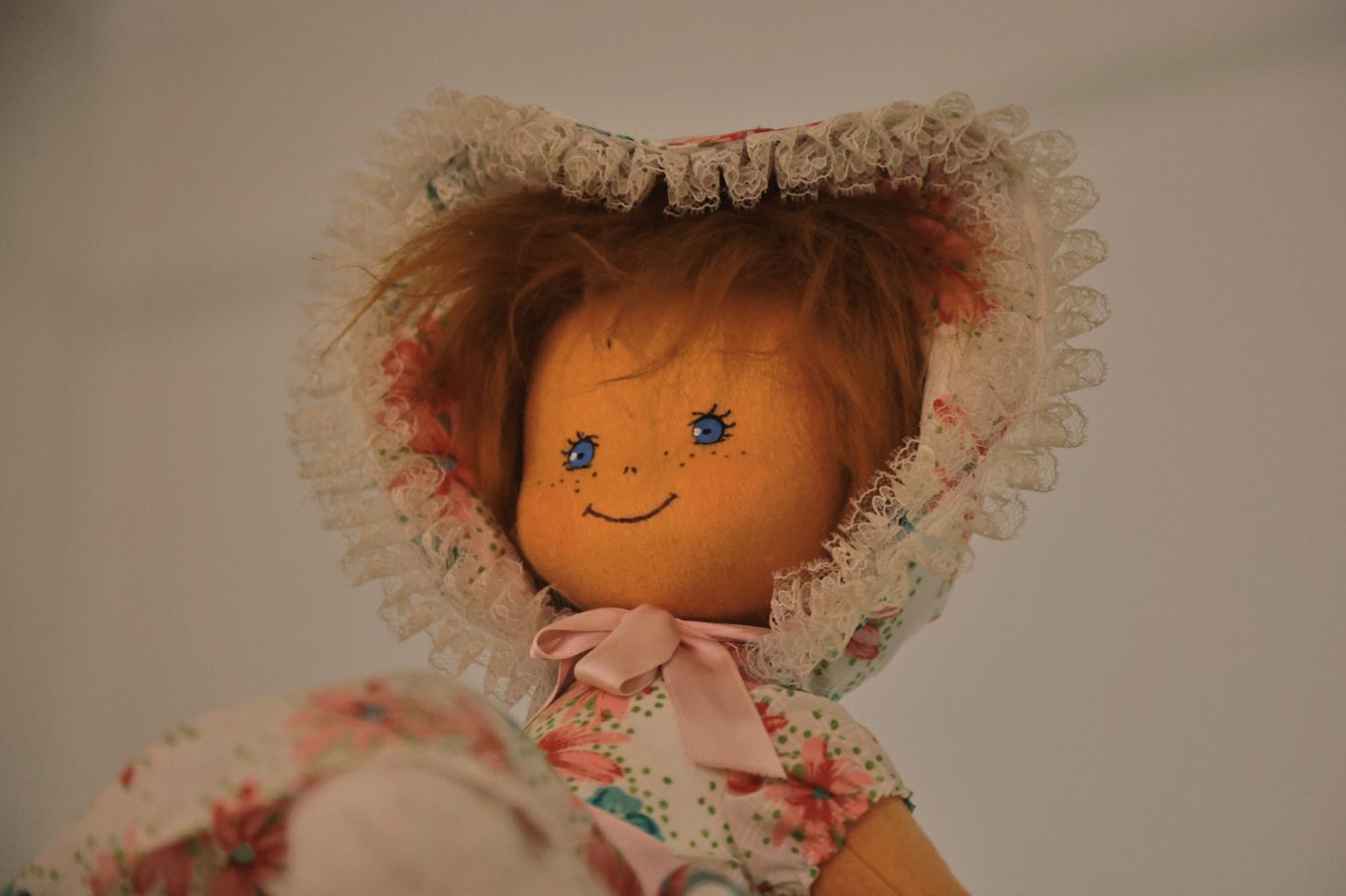 Puppe mit blauen Augen, braunem Haar und einem Blumenmusterkleid mit Haube.