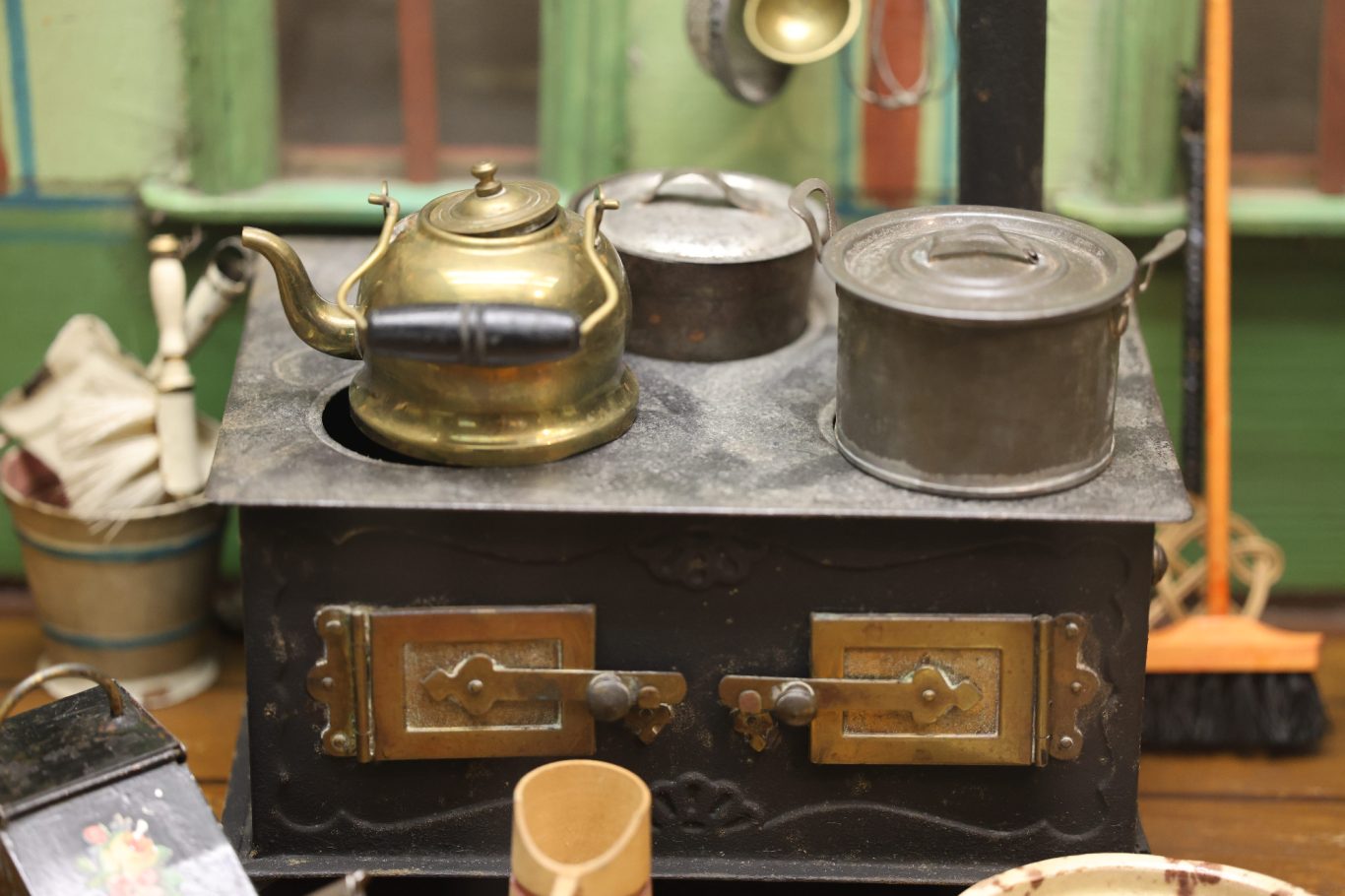 Ein antiker Kochtopf mit Kessel auf einem Holzofen, im Hintergrund Haushaltsgegenstände.