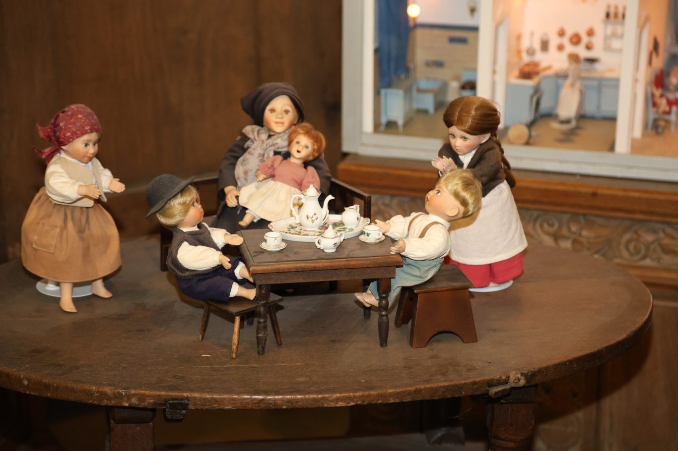 Sechs Puppen sitzen um einen Tisch und genießen eine Teestunde in einem gemütlichen Raum.